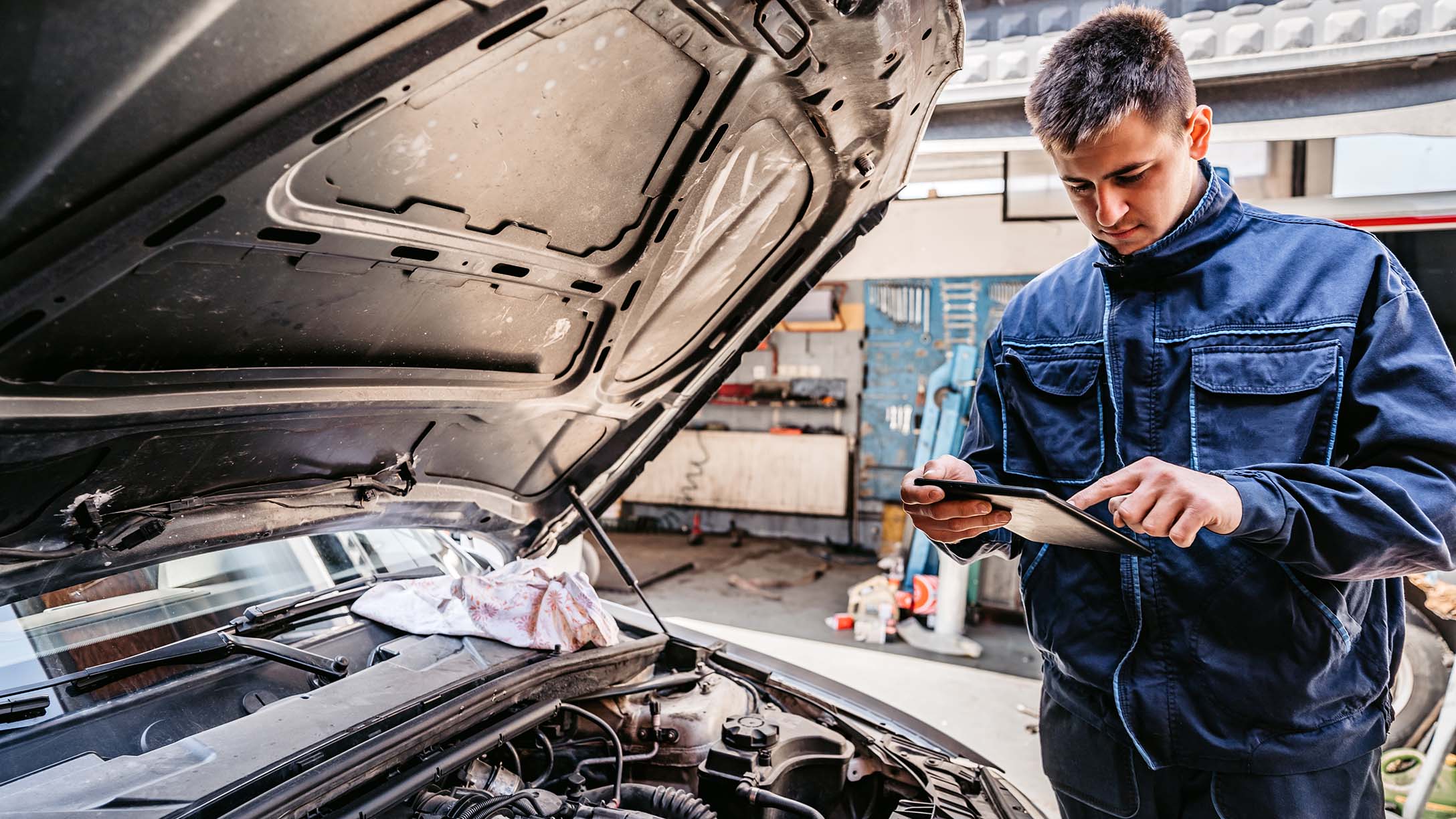 A mechanic looking at iPad near a car engine.