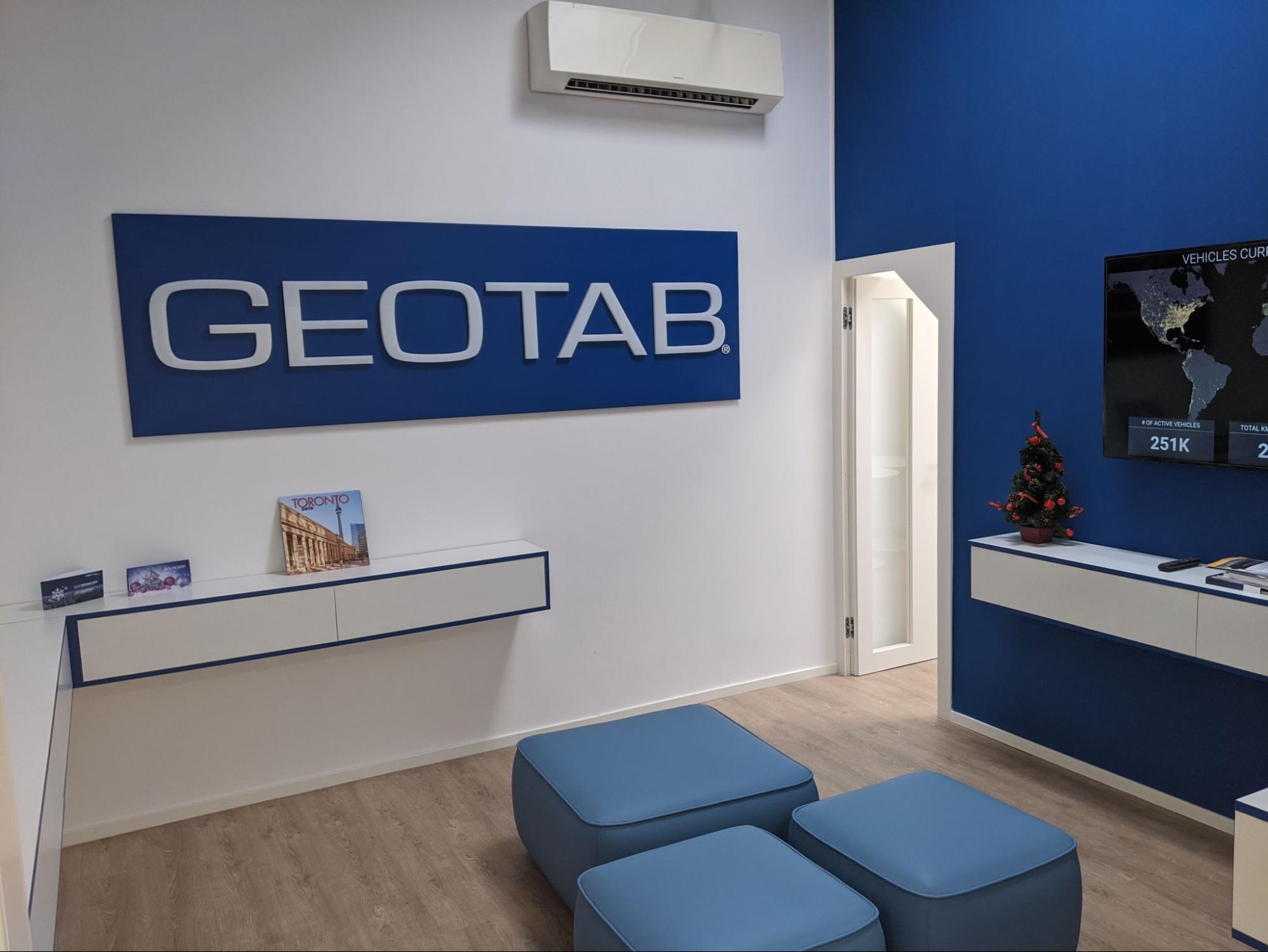 An image of a cozy office room with ottoman chairs and a wall mounted TV in Geotab’s Rome office.