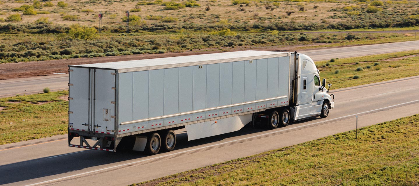 a white fleet truck driving down a one-lane highway surrounded by a field.