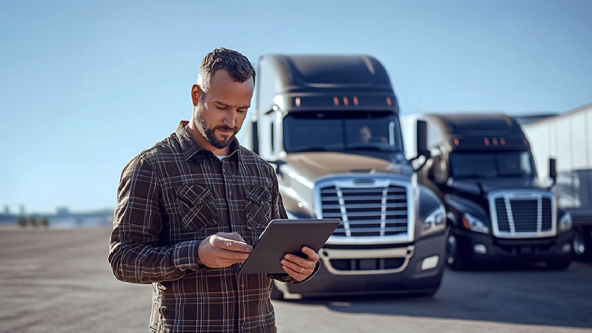 person looking at a tablet with trucks in the background