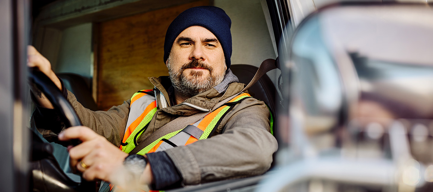 a man wearing a blue beanie and safety vest driving a fleet vehicle.