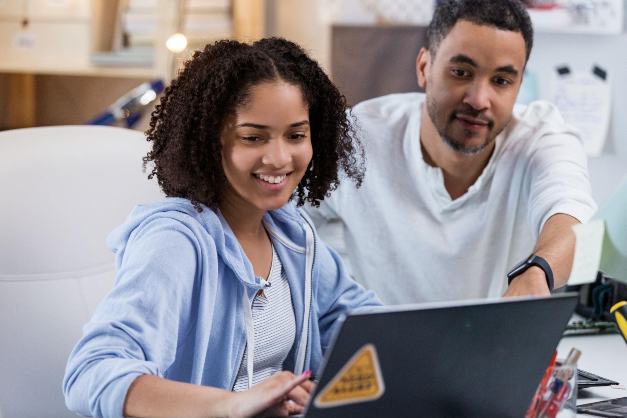 Girl using computer with man pointing towards the screen from her side