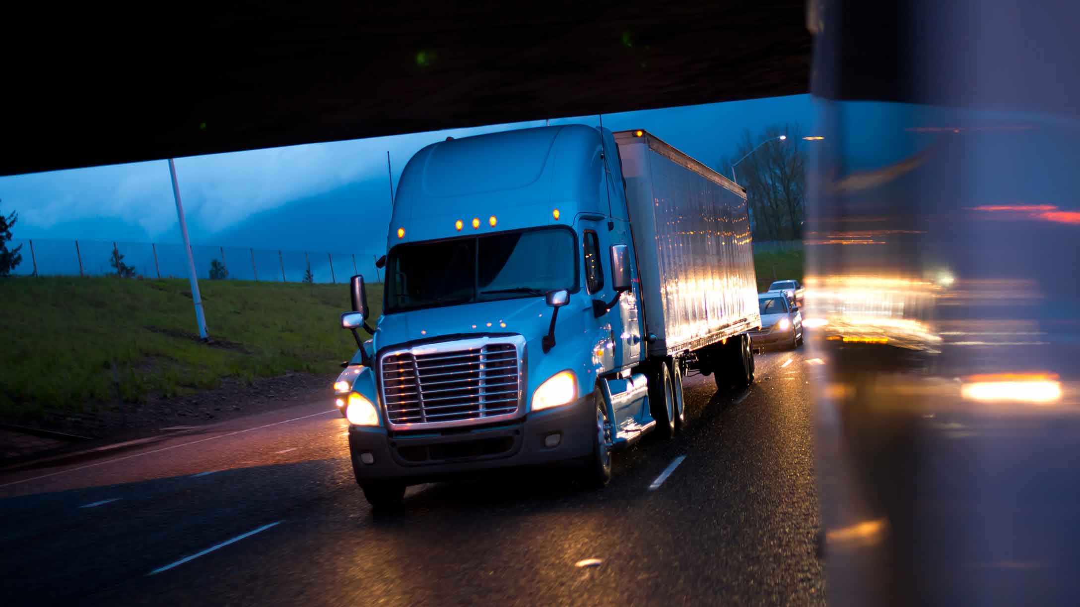 Camión de transporte de carga circulando por una carretera durante la noche, con las luces encendidas, destacando la seguridad en el transporte en condiciones de baja visibilidad.