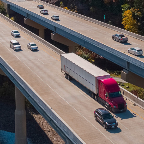 Camión de carga y automóviles circulando en una autopista de dos niveles, representando la gestión y monitoreo de flotas en carretera.