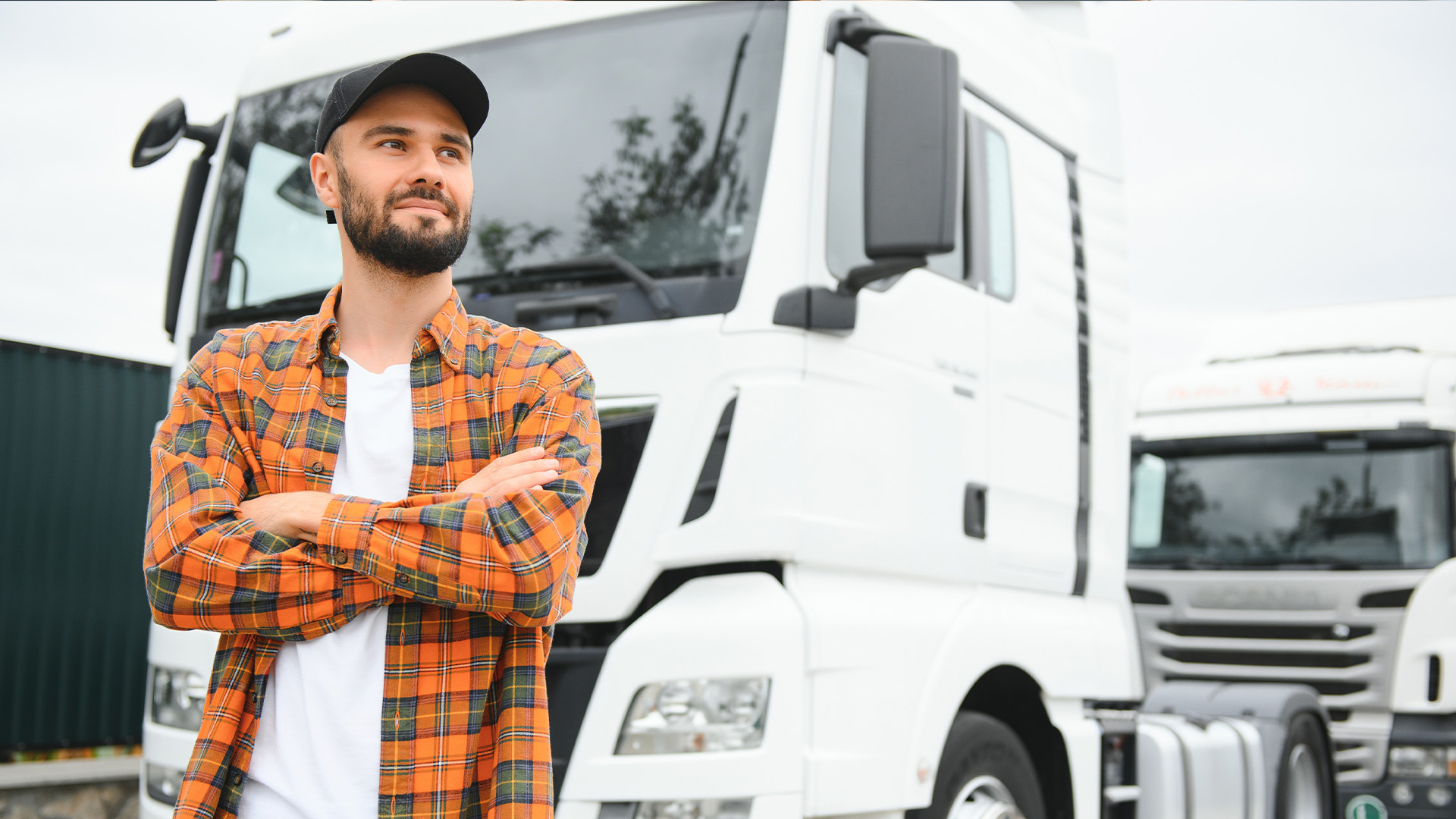 Un conductor mira con orgullo hacia el horizonte, transmitiendo seguridad y tranquilidad. Detrás de él, un vehículo en perfecto estado está listo para iniciar su próximo viaje, lo que demuestra la importancia de la administración de flotas de transporte para garantizar la seguridad y la eficiencia.