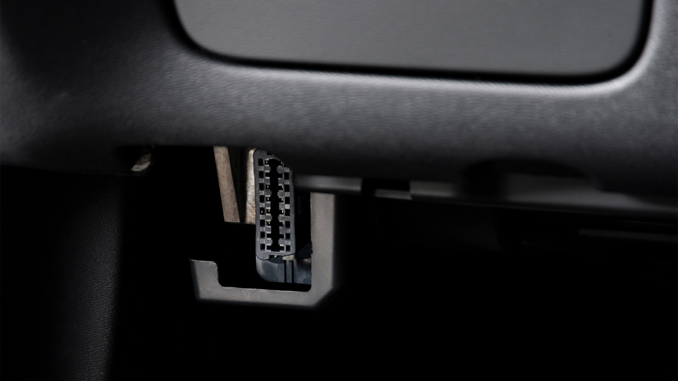 Imagen de un puerto OBD-II (On-Board Diagnostics) ubicado debajo del tablero de un vehículo. Este conector se utiliza para diagnósticos automotrices y acceso a datos en tiempo real del vehículo.