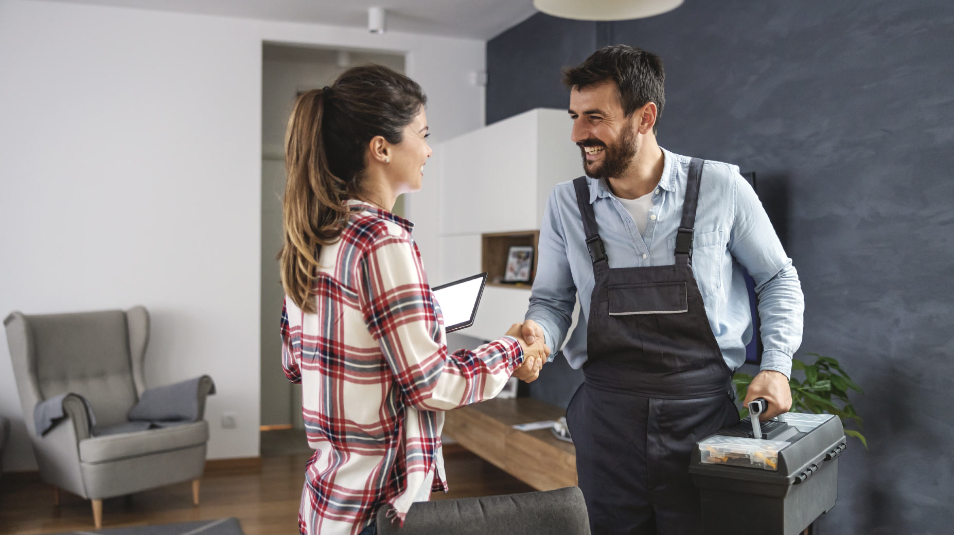 Una clienta saluda con un apretón de manos a un técnico de servicios de campo sonriente, quien lleva una caja de herramientas. La clienta sostiene una tableta, sugiriendo una interacción eficiente y moderna.