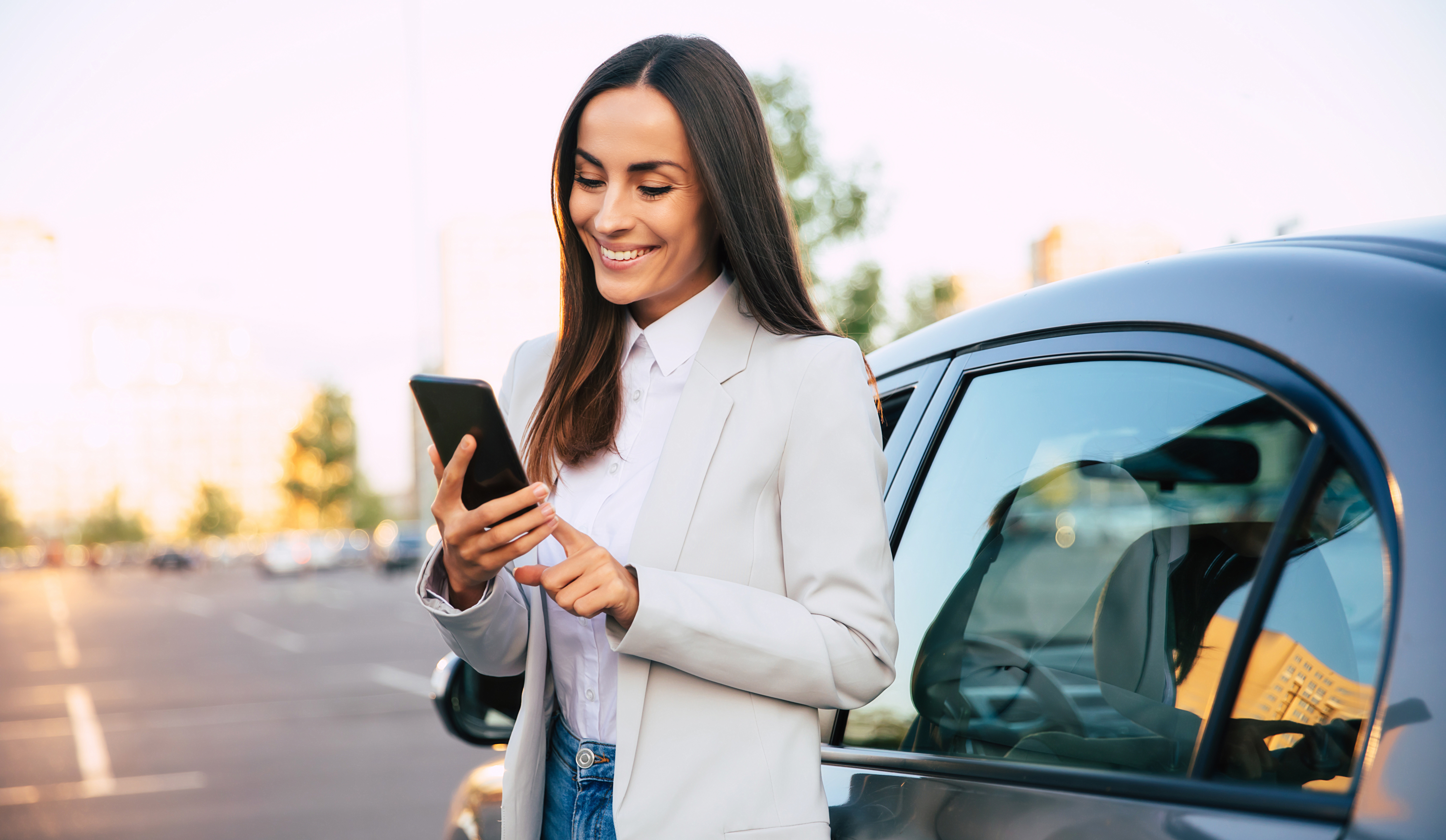Smiling woman using smartphone by car.