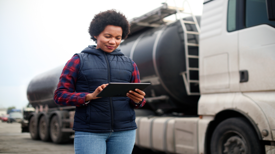 Vrouwelijke vrachtwagenchauffeur of fleetmanager kijkt op een tablet bij haar vrachtwagen.