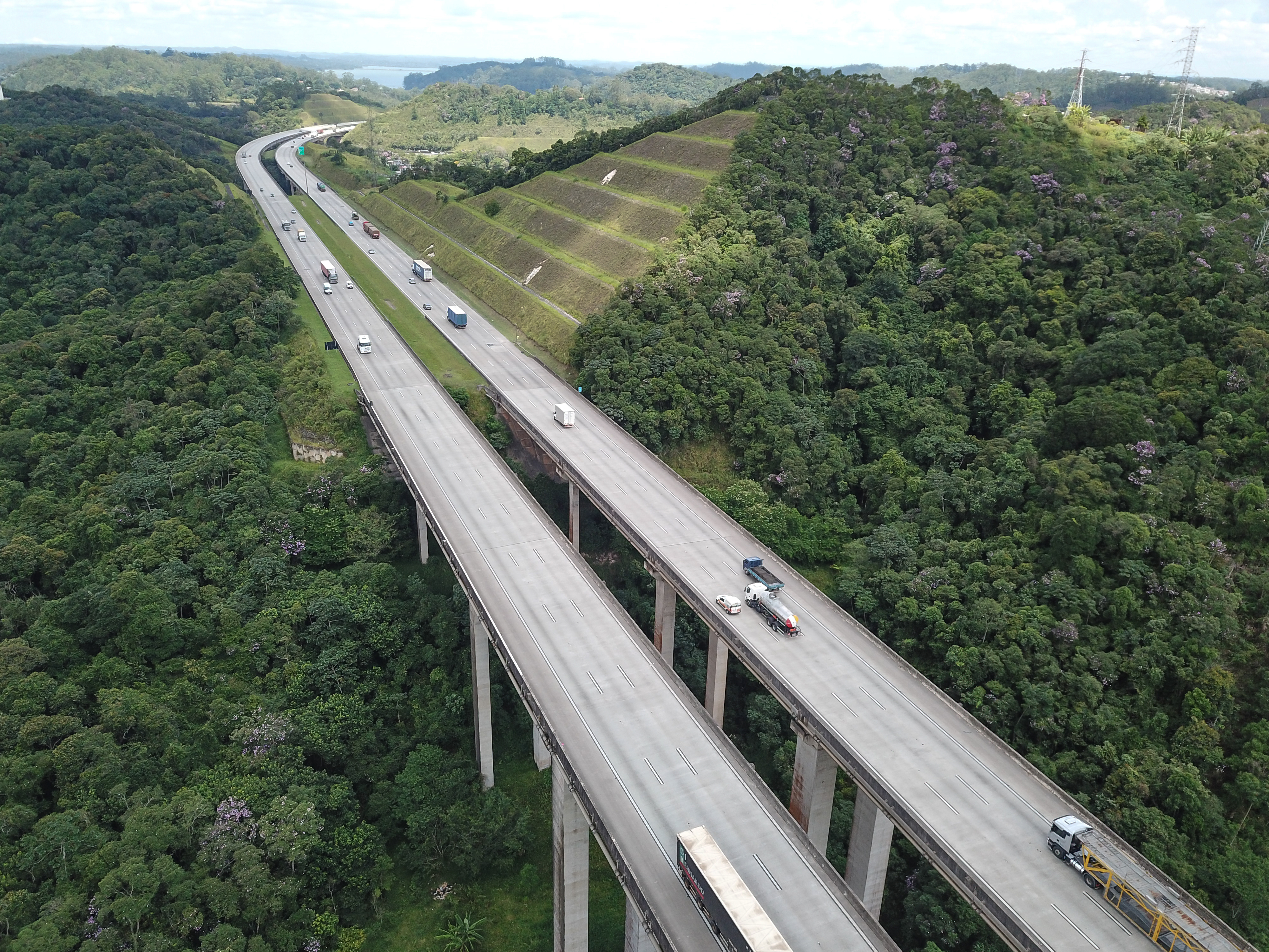 Imagem aérea de uma rodovia movimentada com vários caminhões, representando o fluxo logístico e a importância da conectividade nas estradas.