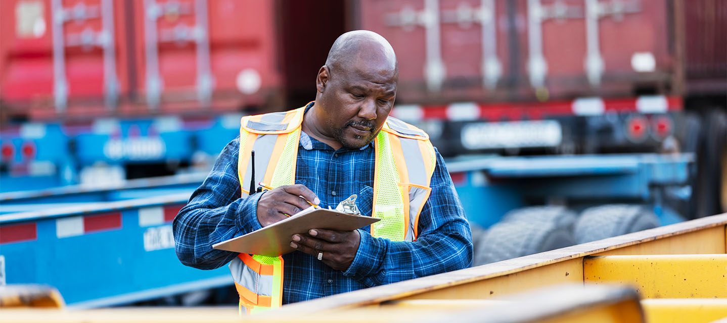 Inspeção de carga por trabalhador em terminal de transporte. Imagem relacionada a custos operacionais e eficiência na gestão de frotas.