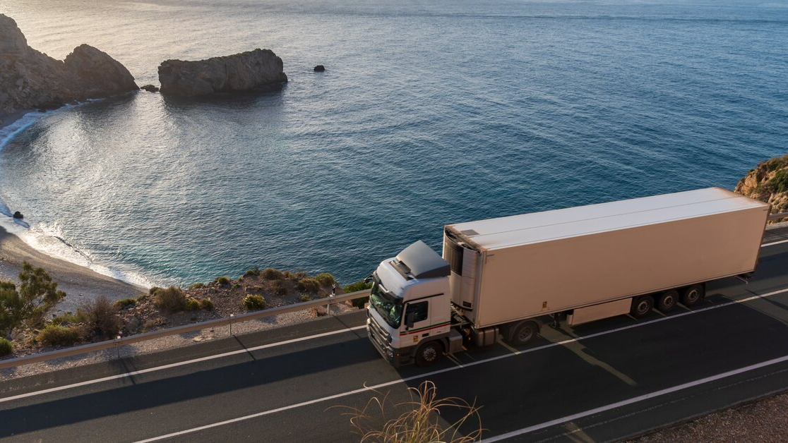 Refrigerated lorry driving along a coastal highway.
