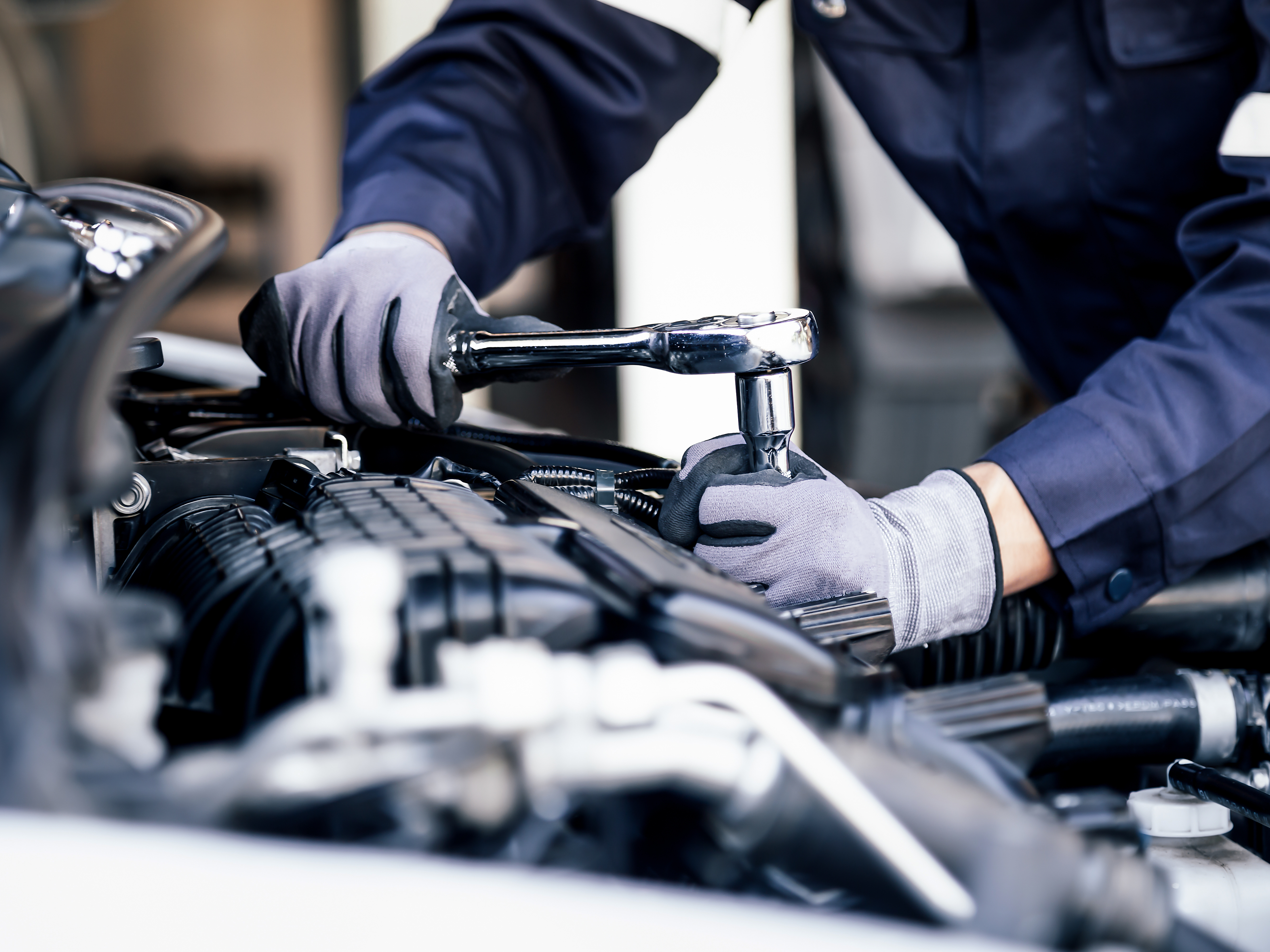 A mechanic in gloves is tightening a bolt on a vehicle engine in a workshop